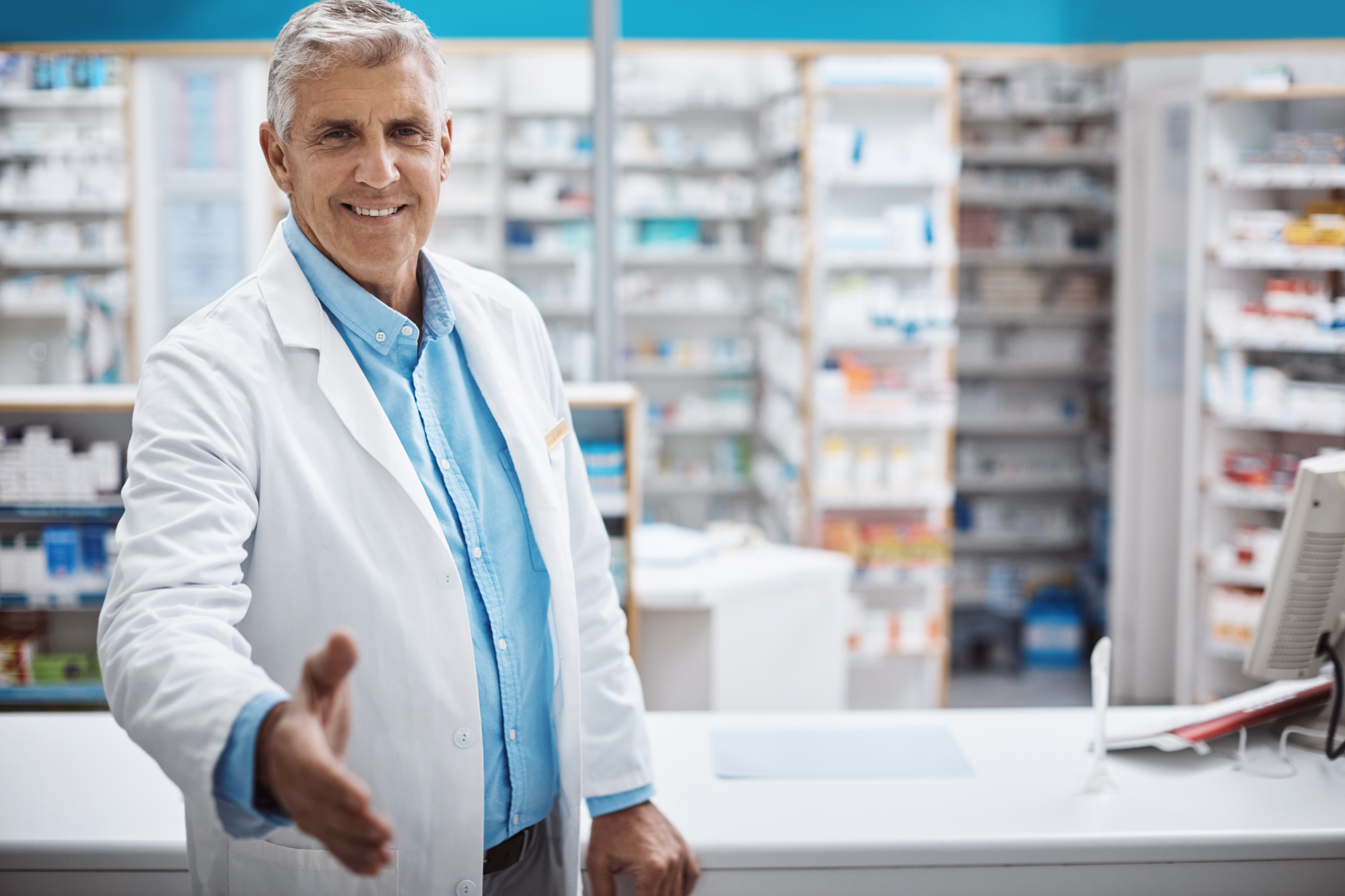 A smiling male pharmacist extends his hand for a handshake.